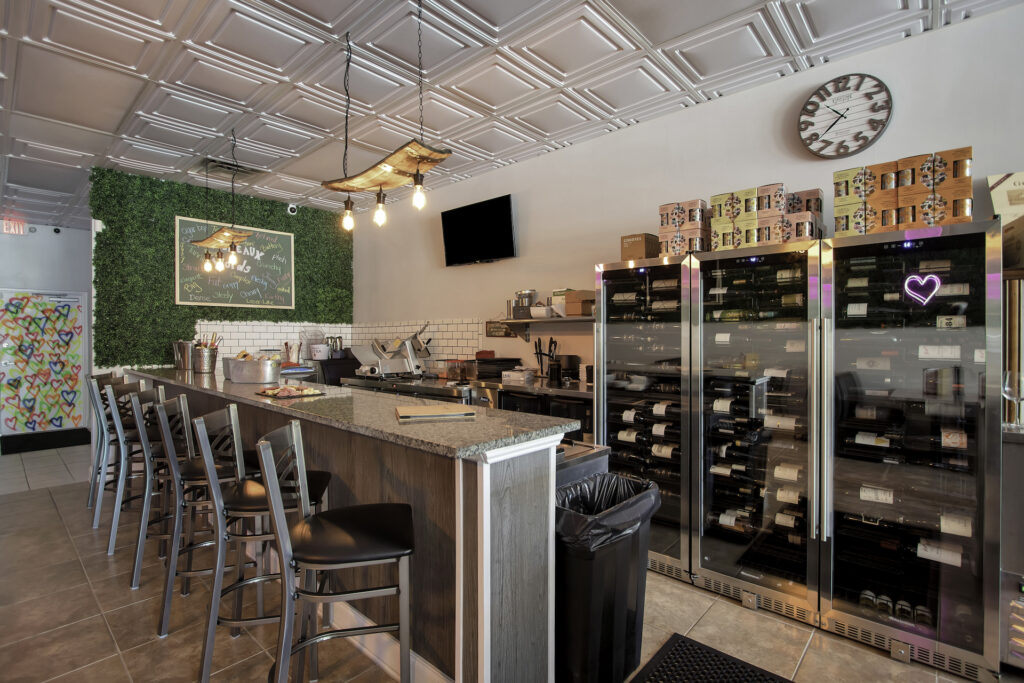 a quaint wine bar with a fridge filled with different bottles of wine and a living plant wall. 