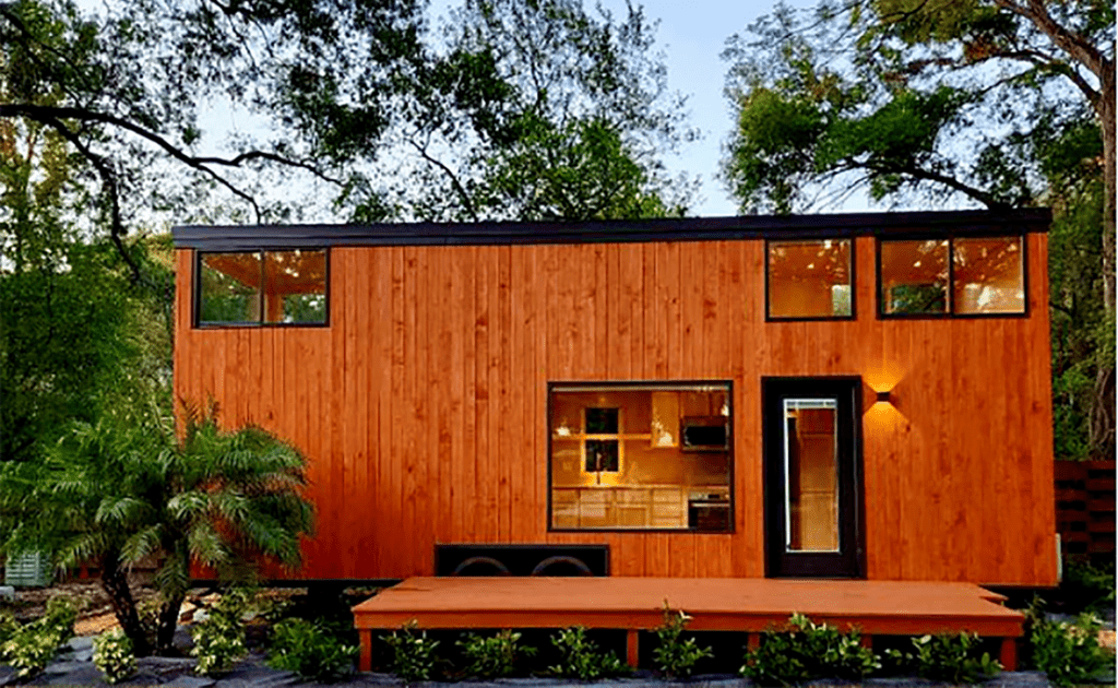 A tiny home with a bright brown wood facade  surrounded by trees. 