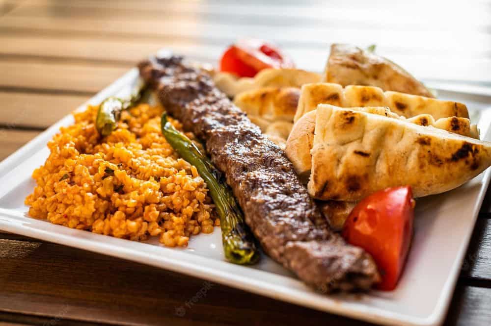 A plate of charred meat, rice, pita and veggies. 