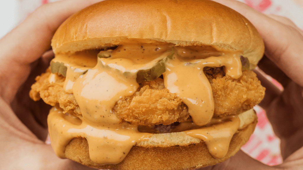 Fried Chicken sandwich, the piece of fried chicken is covered in pickles and a mustard sauce. 