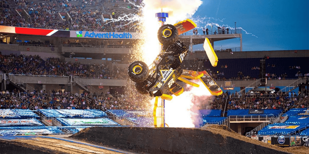 monster truck does a flip in the air with an explosion going off. 